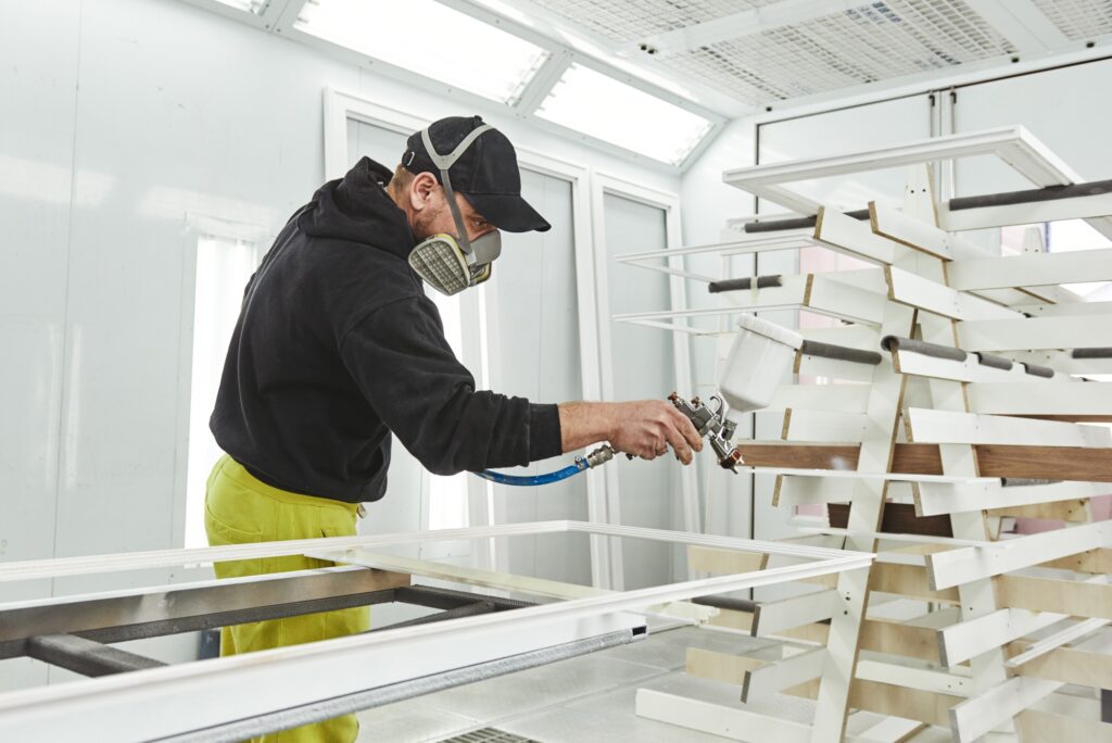Exceptional painting services. Man in respirator mask painting wooden planks at workshop